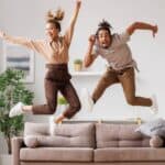 A happy young couple celebrate a win by jumping high above their new sofa.